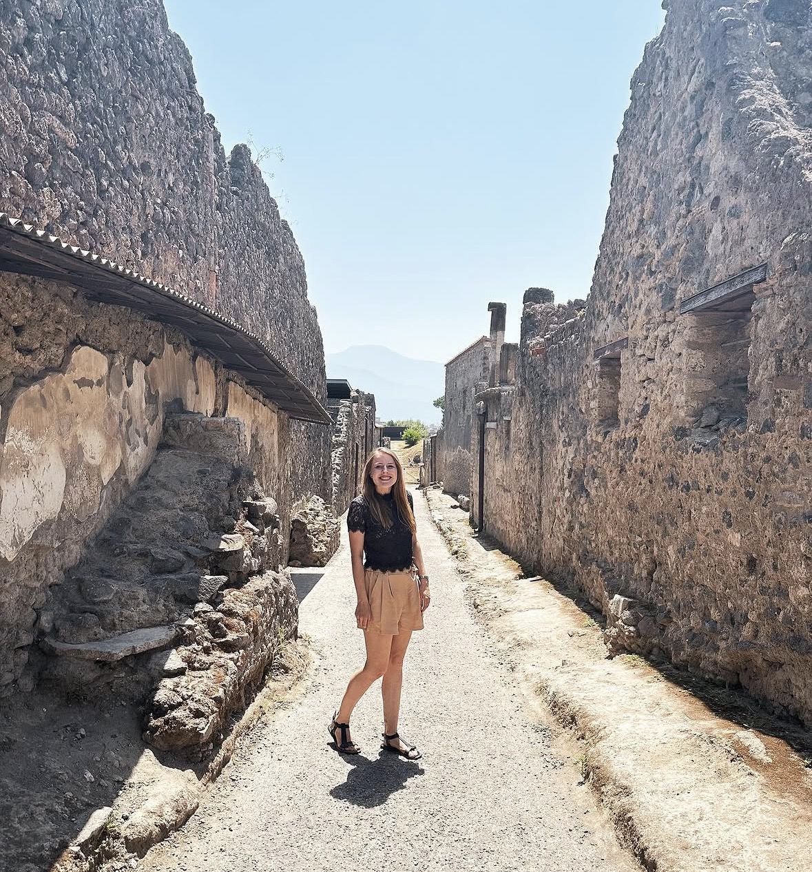 Visitor with comfortable backpack and hat exploring ancient Roman cobblestone streets in bright sunshine